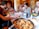 Close-up of a joyful group sharing a pasta meal at a rustic wooden table.