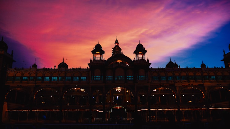 A regal Maharaja in traditional attire overlooking a majestic Indian palace at sunset.