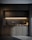 A modern kitchen with dark cabinetry and a sleek, minimalist design. The countertop is made of dark marble, and there's a built-in stove. Under-cabinet lighting provides a warm glow. A knife block and a couple of cutting boards are placed on the counter next to the stove.