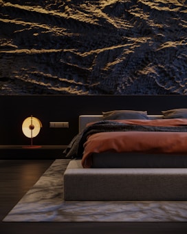 A modern bedroom featuring a textured dark wall with wave-like patterns. The bed has a low-profile design, dressed in dark gray bedding with a burnt orange blanket. A contemporary round lamp with a soft glow sits on a sleek bedside table. The room is minimalistic, with a sense of balance and harmony.