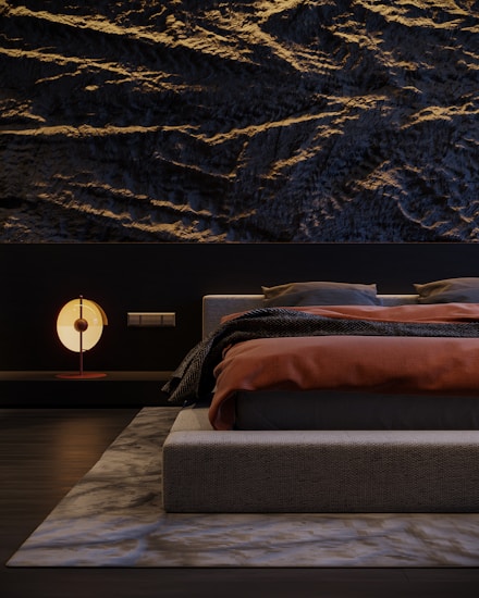 A modern bedroom featuring a textured dark wall with wave-like patterns. The bed has a low-profile design, dressed in dark gray bedding with a burnt orange blanket. A contemporary round lamp with a soft glow sits on a sleek bedside table. The room is minimalistic, with a sense of balance and harmony.