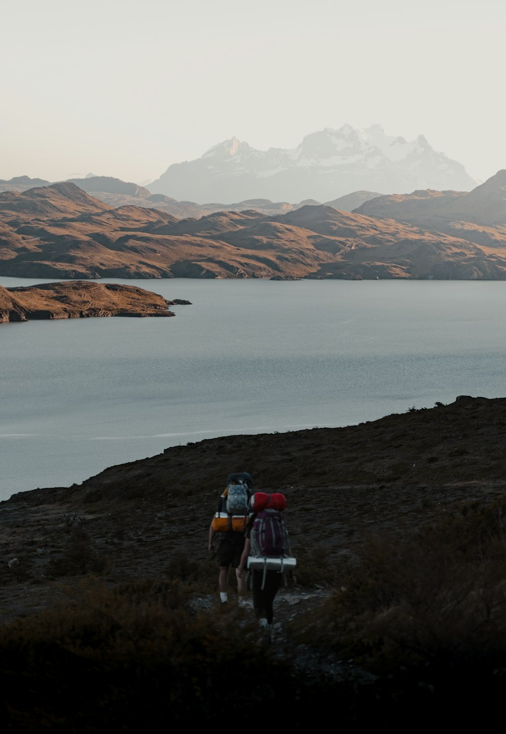 a couple people walking on a rocky shore by a body of water