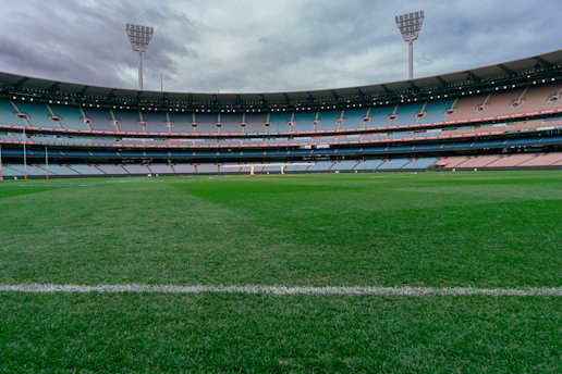 The Melbourne Cricket Ground with empty tiered seating under a cloudy sky in Melbourne