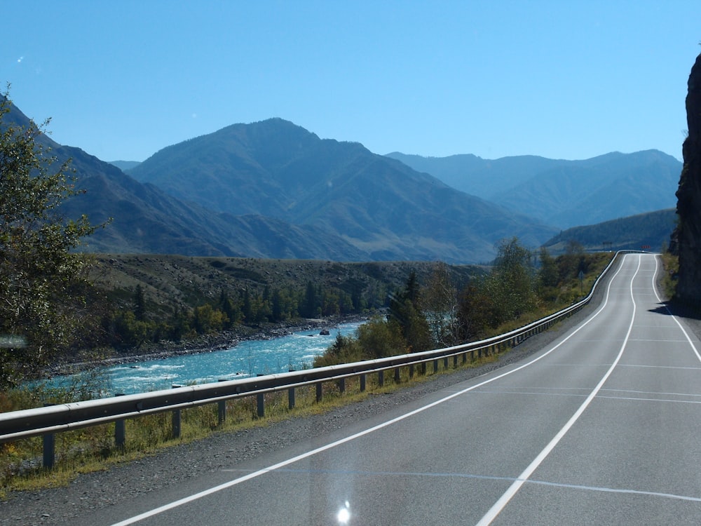 a road with a body of water and trees on the side