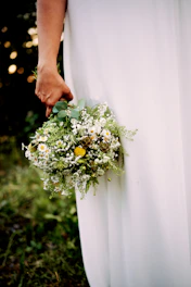 Sunlit bridal bouquet with soft sand and terracotta blooms in a candid outdoor setting.