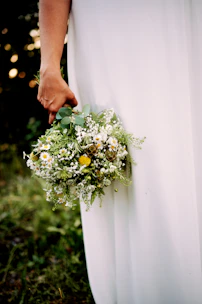 Sunlit bridal bouquet with soft sand and terracotta blooms in a candid outdoor setting.