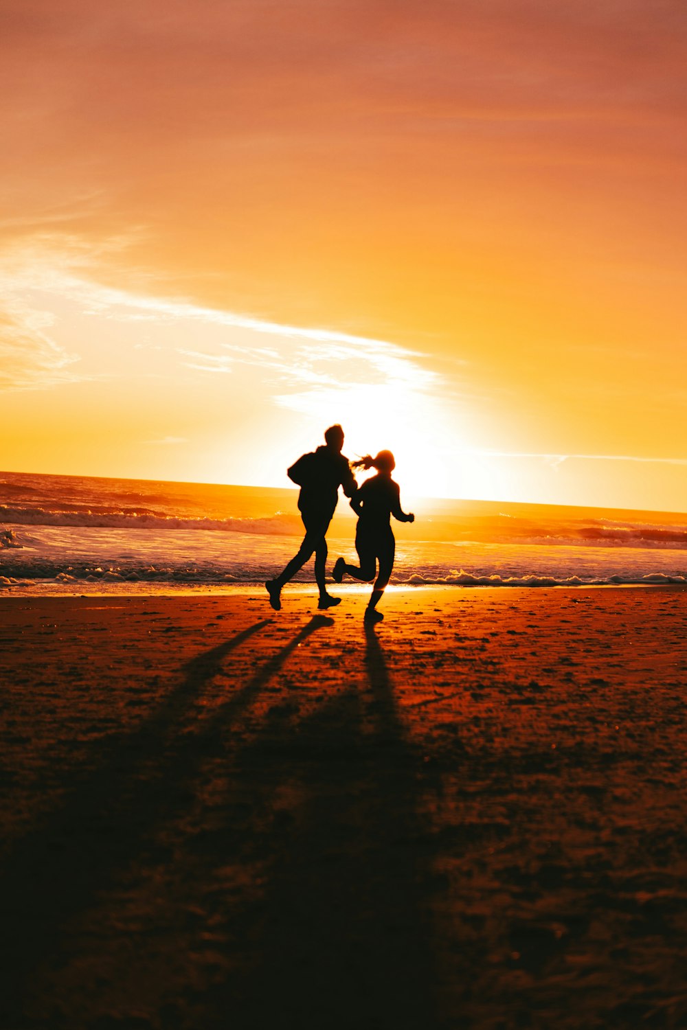 a couple of people running on a beach at sunset