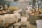Inside a cheese production facility, two workers wearing white uniforms and caps are tending to large copper vats used for cheese making. Several containers wrapped in cloth are visible on tables and carts, with industrial equipment and pipes lining the walls. The space is clean and organized, reflecting an industrial setting.