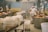 Inside a cheese production facility, two workers wearing white uniforms and caps are tending to large copper vats used for cheese making. Several containers wrapped in cloth are visible on tables and carts, with industrial equipment and pipes lining the walls. The space is clean and organized, reflecting an industrial setting.
