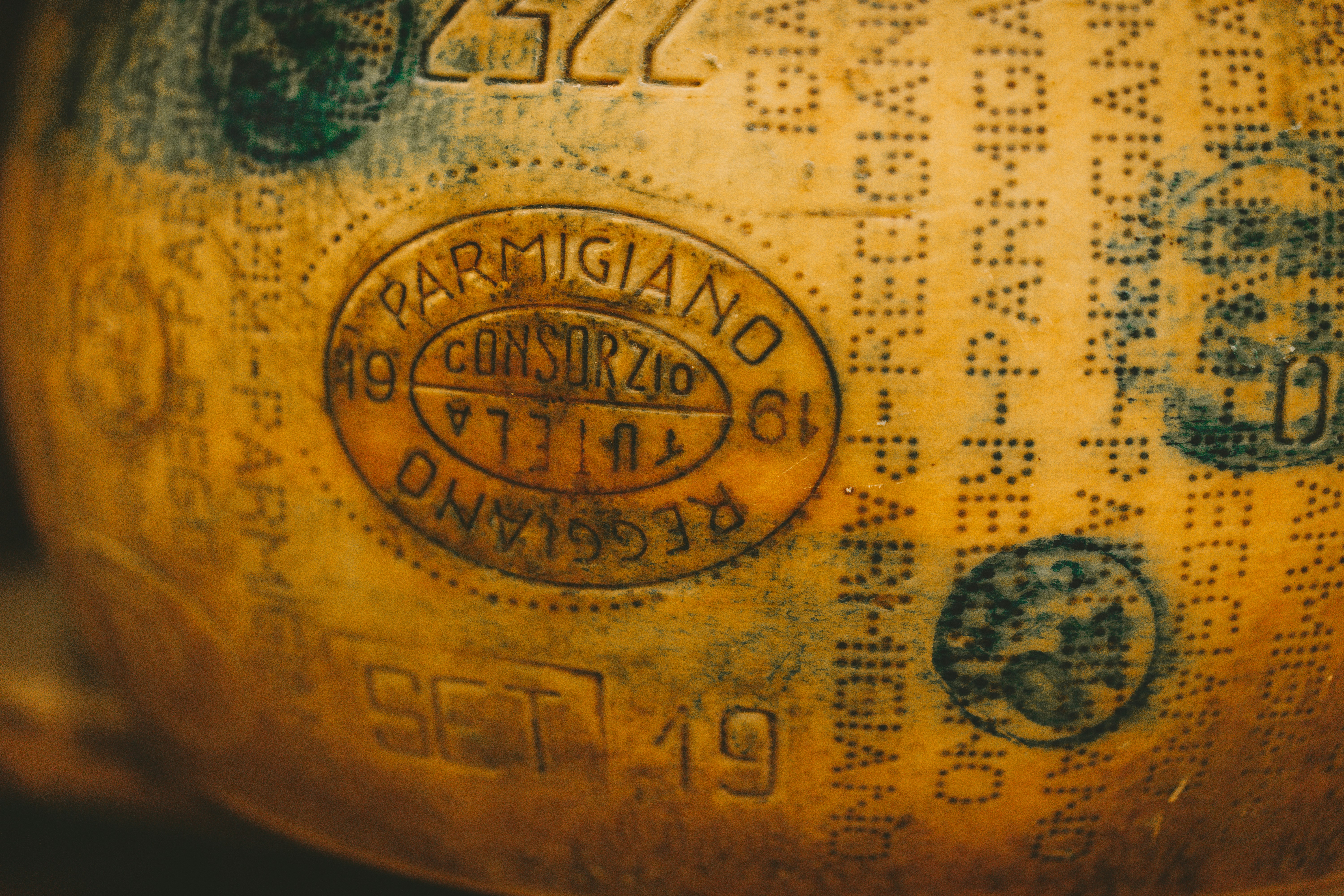 Close-up of the stamped rind of a Parmigiano Reggiano wheel being broken open with a traditional knife