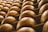 Rows of large, round cheese wheels are stacked on wooden shelves, creating a repetitive geometric pattern. The surface of the cheese has a warm, golden-brown hue and is marked with engraved text.