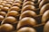 Rows of large, round cheese wheels are stacked on wooden shelves, creating a repetitive geometric pattern. The surface of the cheese has a warm, golden-brown hue and is marked with engraved text.