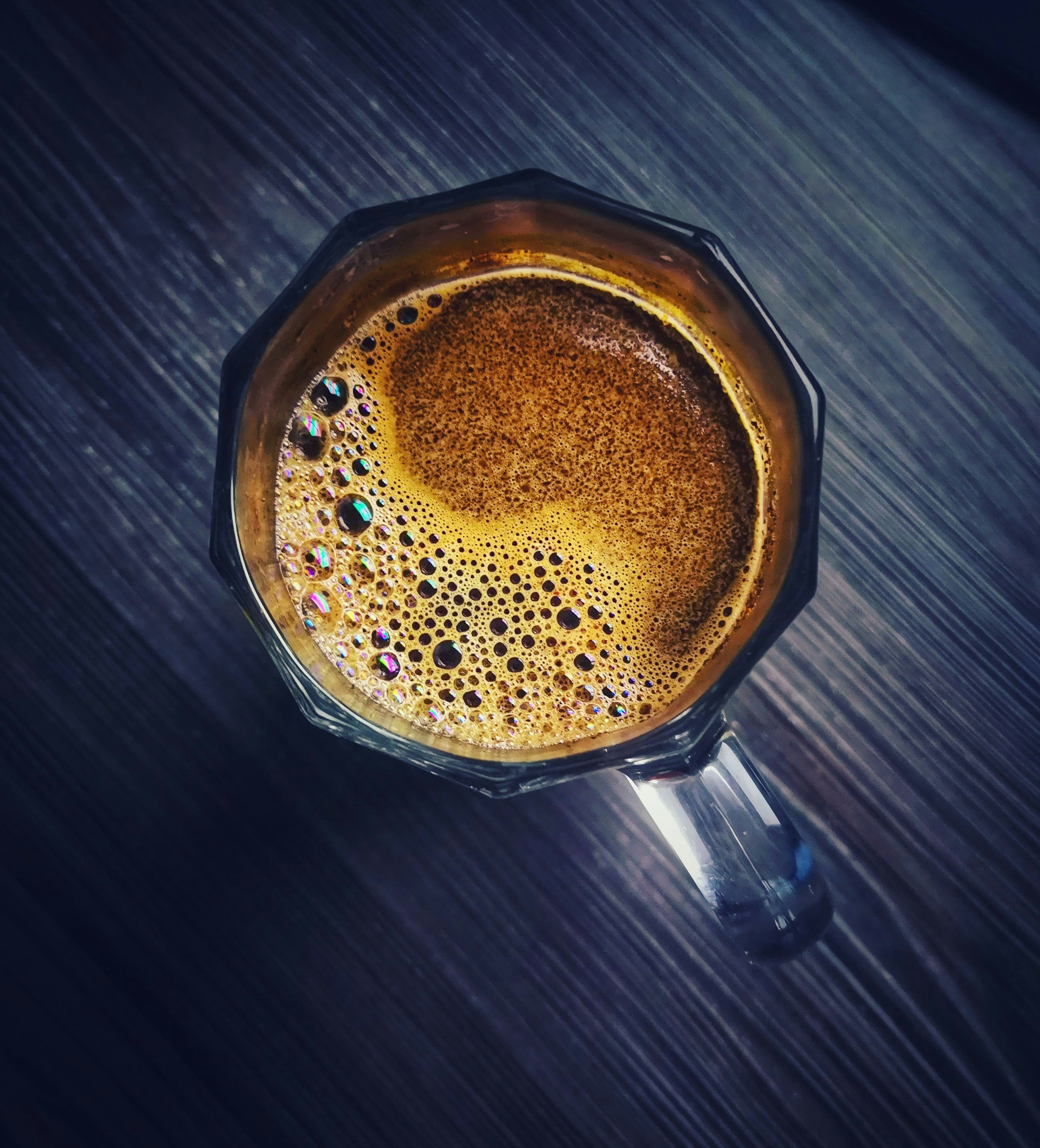 Coffee being poured into ceramic mug from above, warm amber liquid, dark moody kitchen surface, morning light