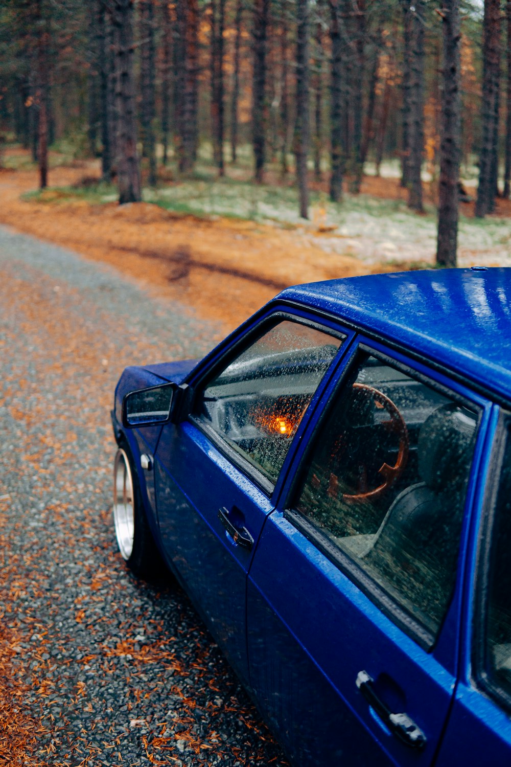 a blue car on a road with trees on either side of it