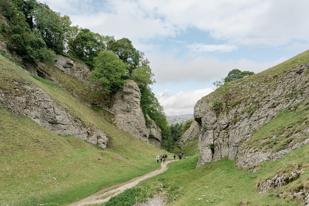 un grupo de personas caminando por un sendero entre colinas rocosas con Winnats Pass al fondo