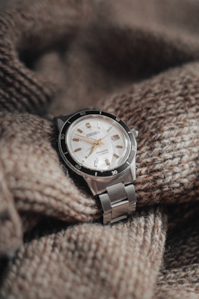 Close-up of a black Timely Grace watch resting on a cozy knitted sweater, showcasing the small round dial.