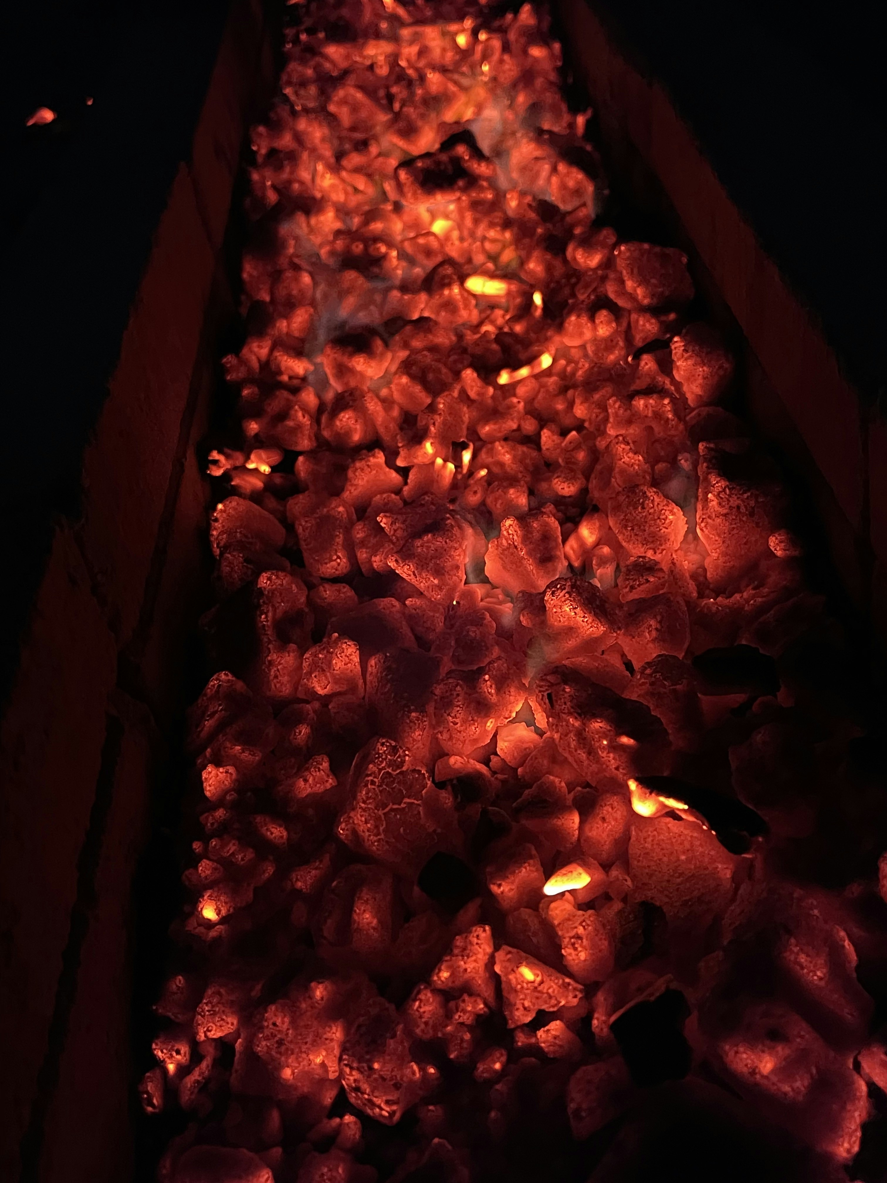Boerewors coil grilling on braai with glowing charcoal embers in dark smoky environment