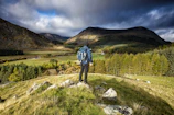 A traveler with a backpack standing on a mountain peak overlooking a valley.