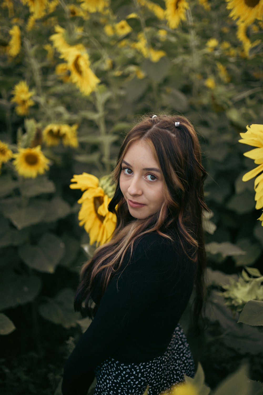 a woman posing in front of a bush of yellow flowers