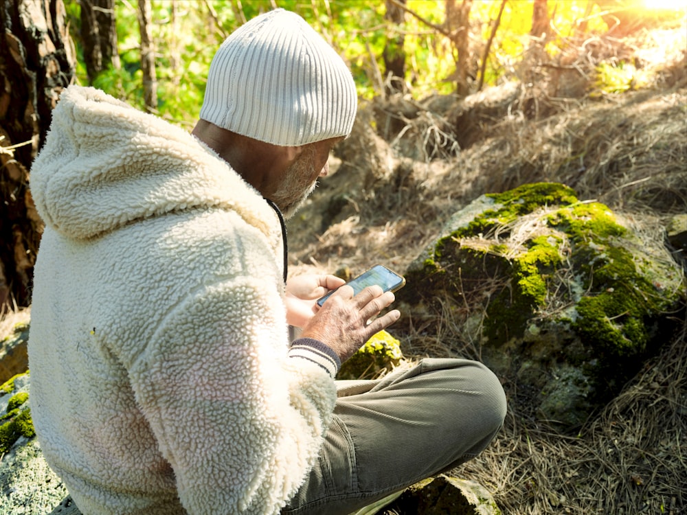 a person sitting on a rock looking at a cell phone