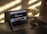 A laptop displaying a webpage sits on a dark table with an open internet browser. Beside the laptop is a transparent vase filled with white flowers. A smartphone lies next to the vase, reflecting the shadows and light on the table.