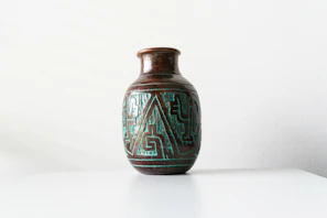 Close-up of a vibrant ceramic vase with geometric patterns, sitting on a dark forest green shelf.