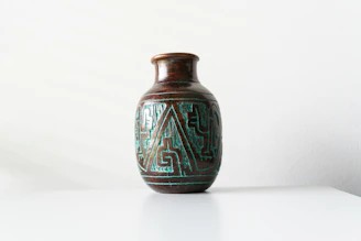 Close-up of a handcrafted terracotta vase with delicate painted details on a neutral background