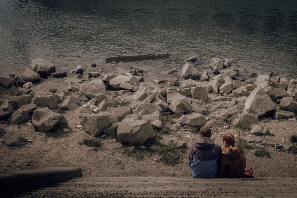 a couple sitting on rocks by the water