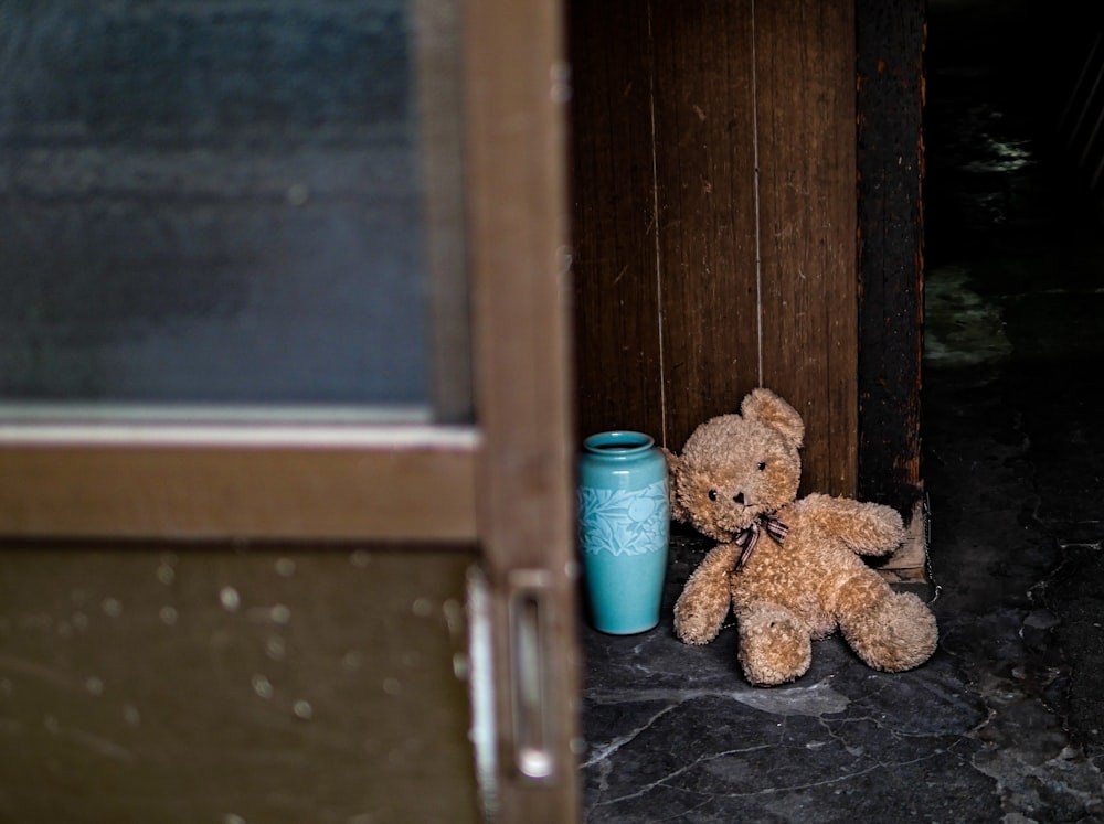 a teddy bear sits next to a blue vase