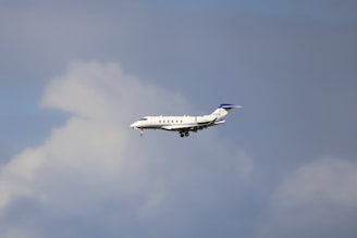 A mid-sized private jet flying through a cloudy sky, showing its landing gear extended.