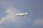 A mid-sized private jet flying through a cloudy sky, showing its landing gear extended.
