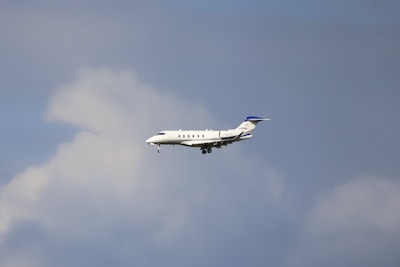 A mid-sized private jet flying through a cloudy sky, showing its landing gear extended.