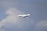A mid-sized private jet flying through a cloudy sky, showing its landing gear extended.