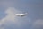 A mid-sized private jet flying through a cloudy sky, showing its landing gear extended.