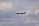 A sleek private jet is flying through a cloudy sky. The aircraft is dark in color and its landing gear is extended. The clouds vary from white to gray, creating a dramatic backdrop.