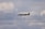 A sleek private jet is flying through a cloudy sky. The aircraft is dark in color and its landing gear is extended. The clouds vary from white to gray, creating a dramatic backdrop.