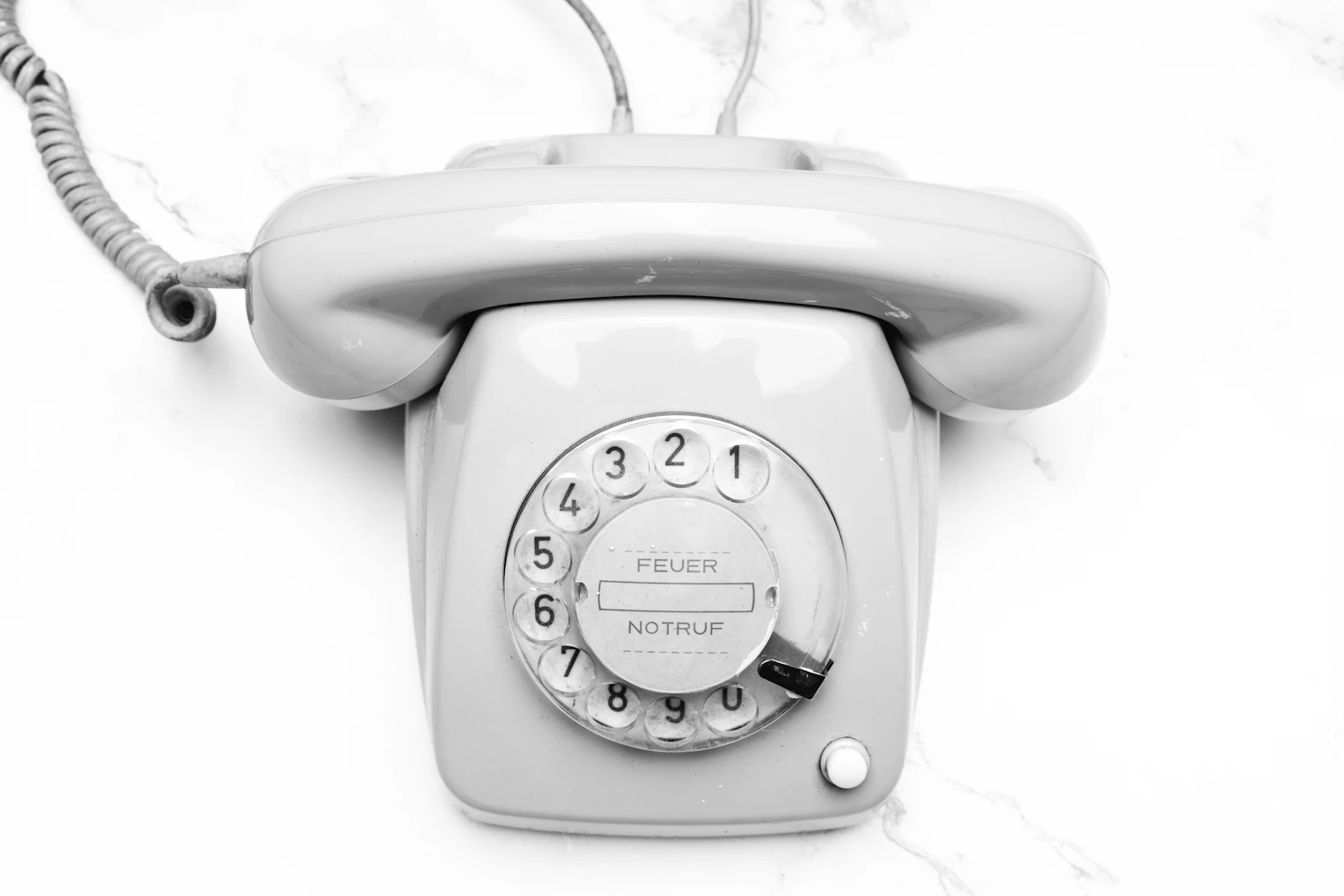 A white rotary telephone on a pale marble surface