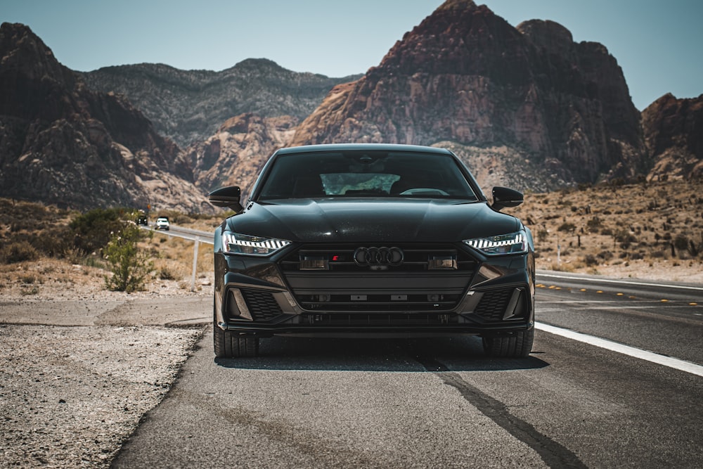 a black car on a road with mountains in the background