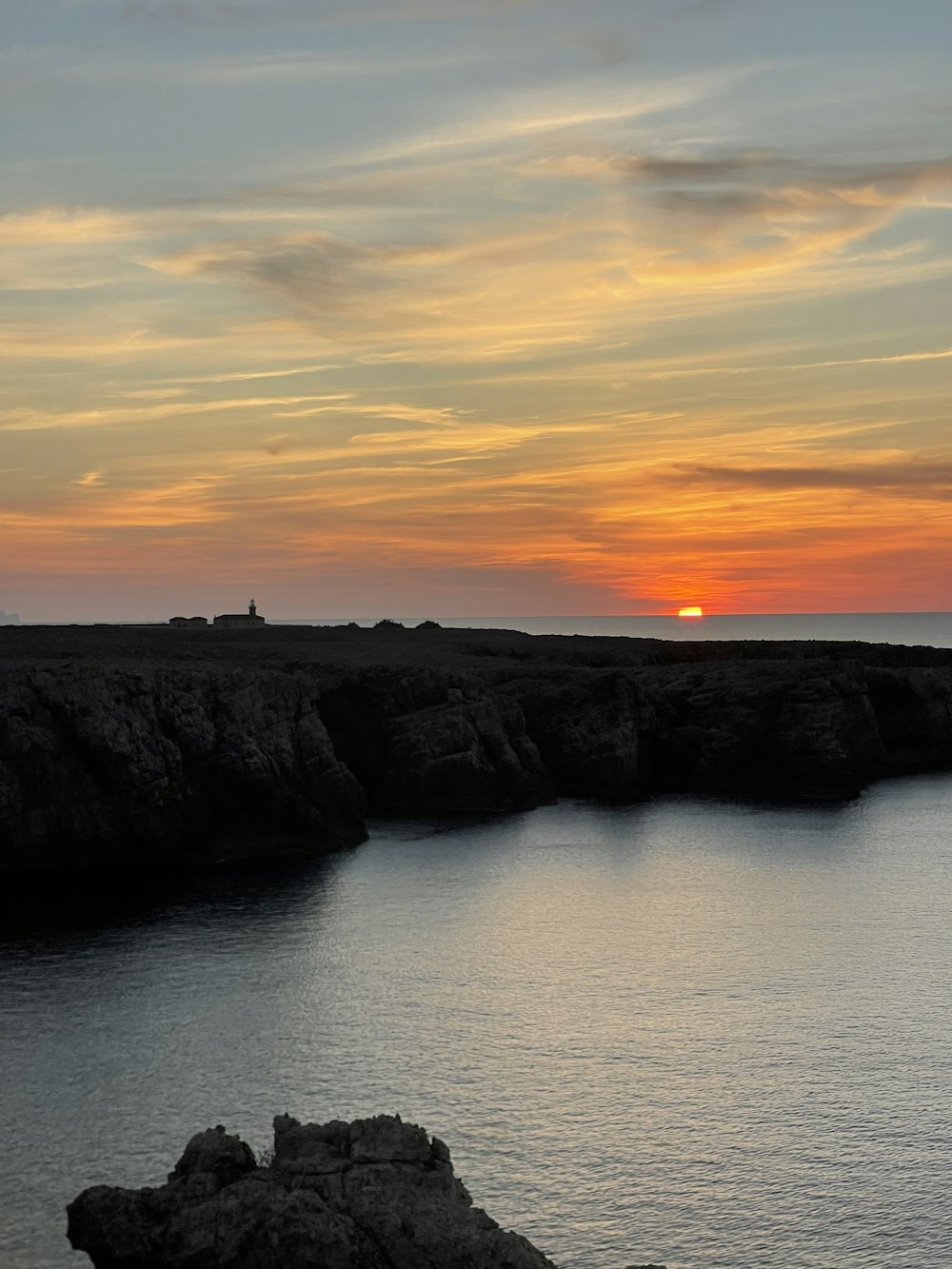 a body of water with a rocky shoreline and a sunset