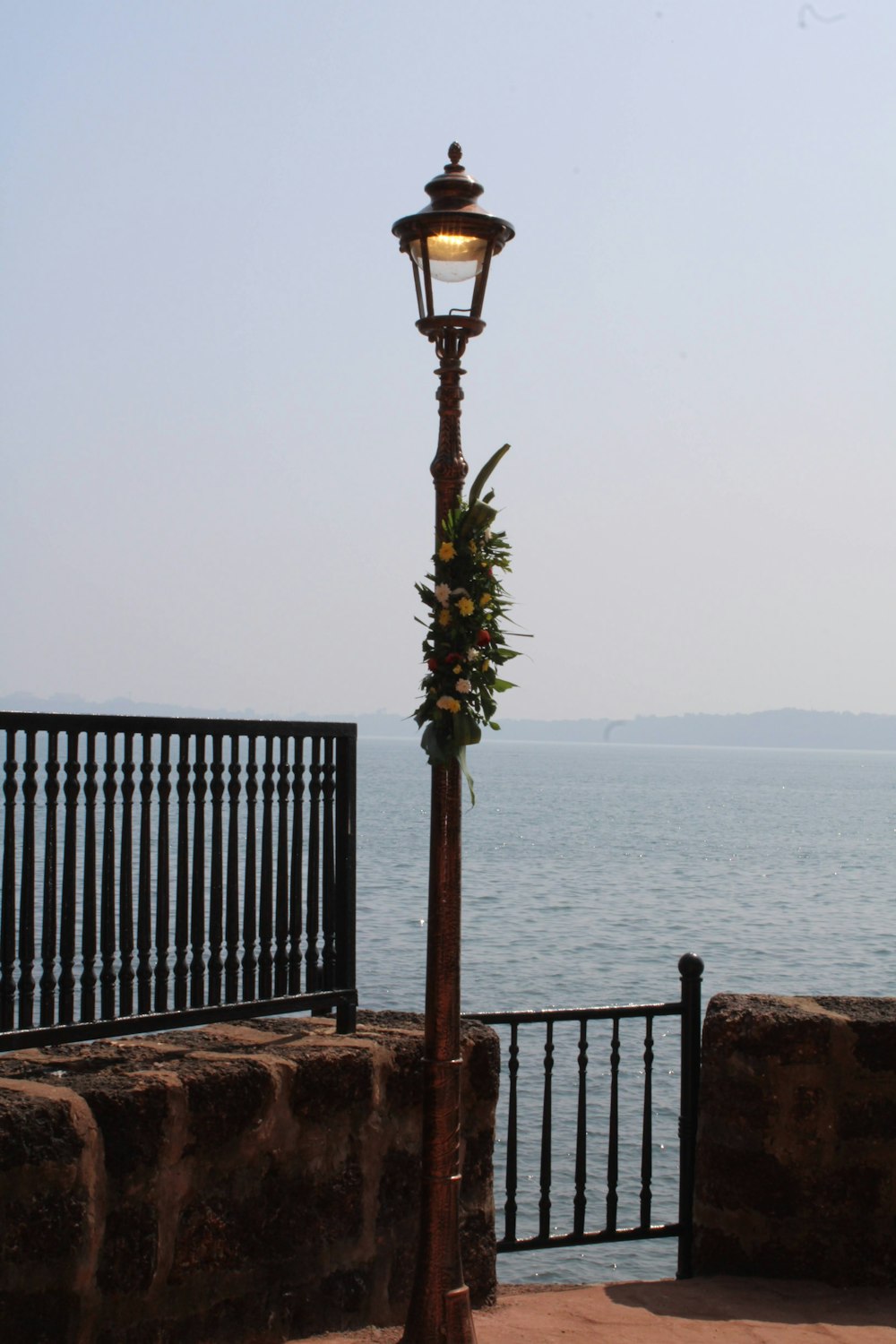 a lamp post on a stone wall by a body of water