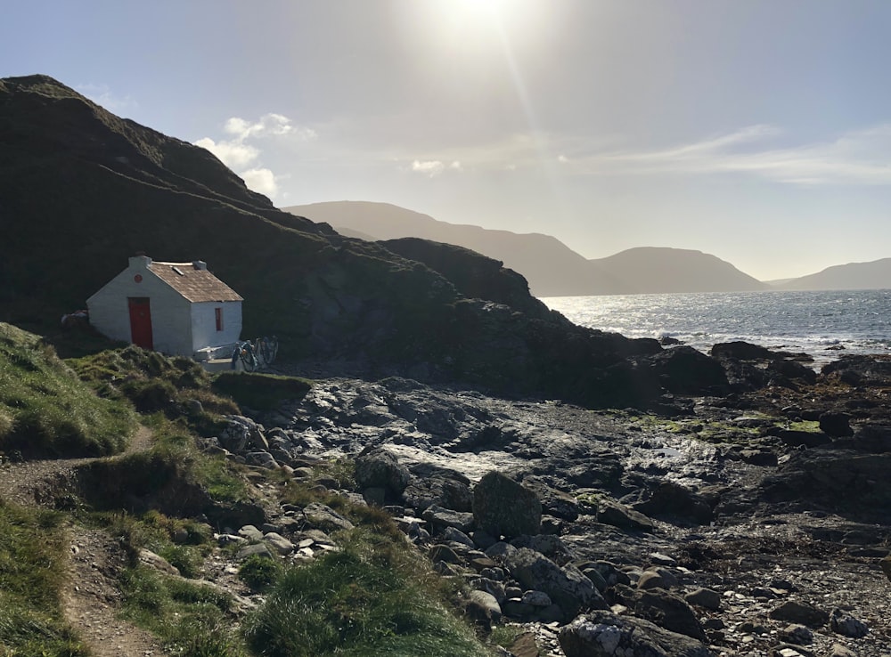 a small white house on a rocky hillside by the water