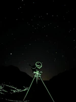 The silhouette of a telescope pointed towards a sparkling cluster of stars.