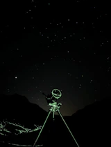 Starry night sky with a silhouette of a robotic rover under a telescope.