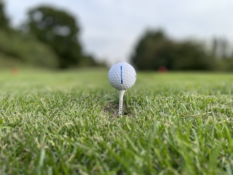Close-up of a golf ball teed up with a luxury home in the background.