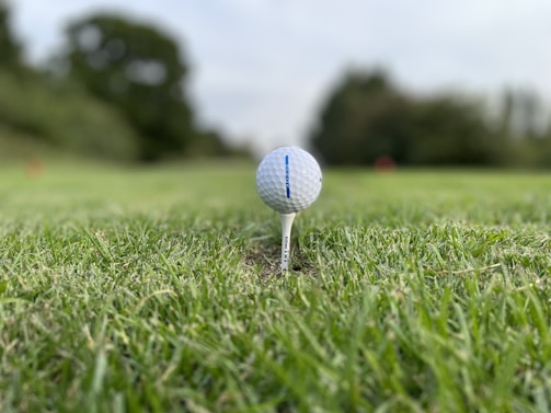 A crisp photo of a golf ball resting on a tee with a luxury home blurred in the background.