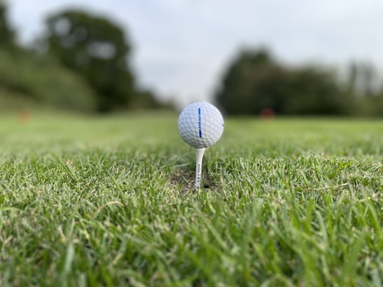 Close-up of a golf ball resting on a tee with a scenic fairway in the background.
