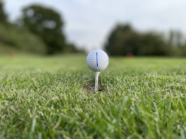A close-up of a golf ball on a tee with a blurred background of a golf course.