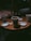 Several disposable coffee cups are placed on a wooden table in what appears to be a dimly lit cafe. The cups have lids nearby, and there are sugar packets and stirrers scattered on the table surface. The lighting creates a cozy and intimate atmosphere.