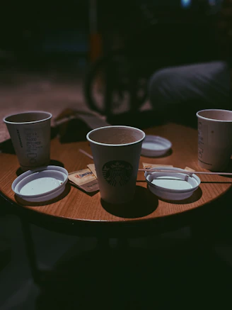Close-up of a steaming cup of coffee next to disposable cups and plates on a wooden table
