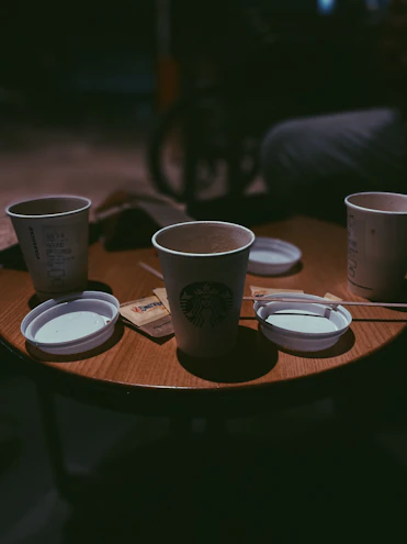 Close-up of a steaming cup of coffee next to disposable cups and plates on a wooden table